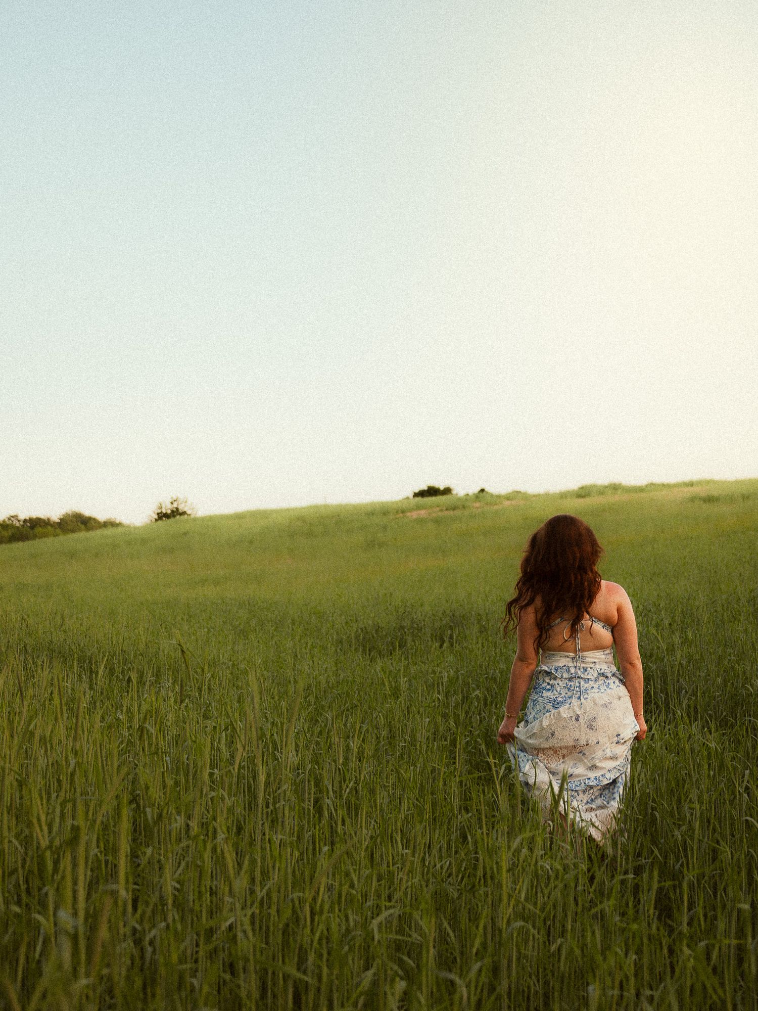 Woman in floral dress walking through lush green field on a sunny day.