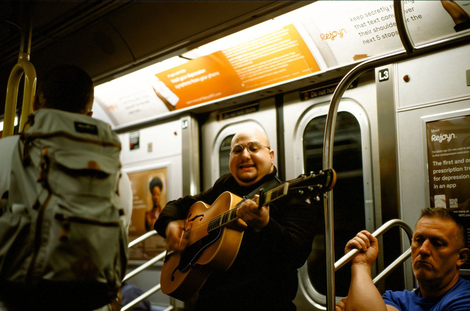 Musician playing acoustic guitar inside a subway car.
