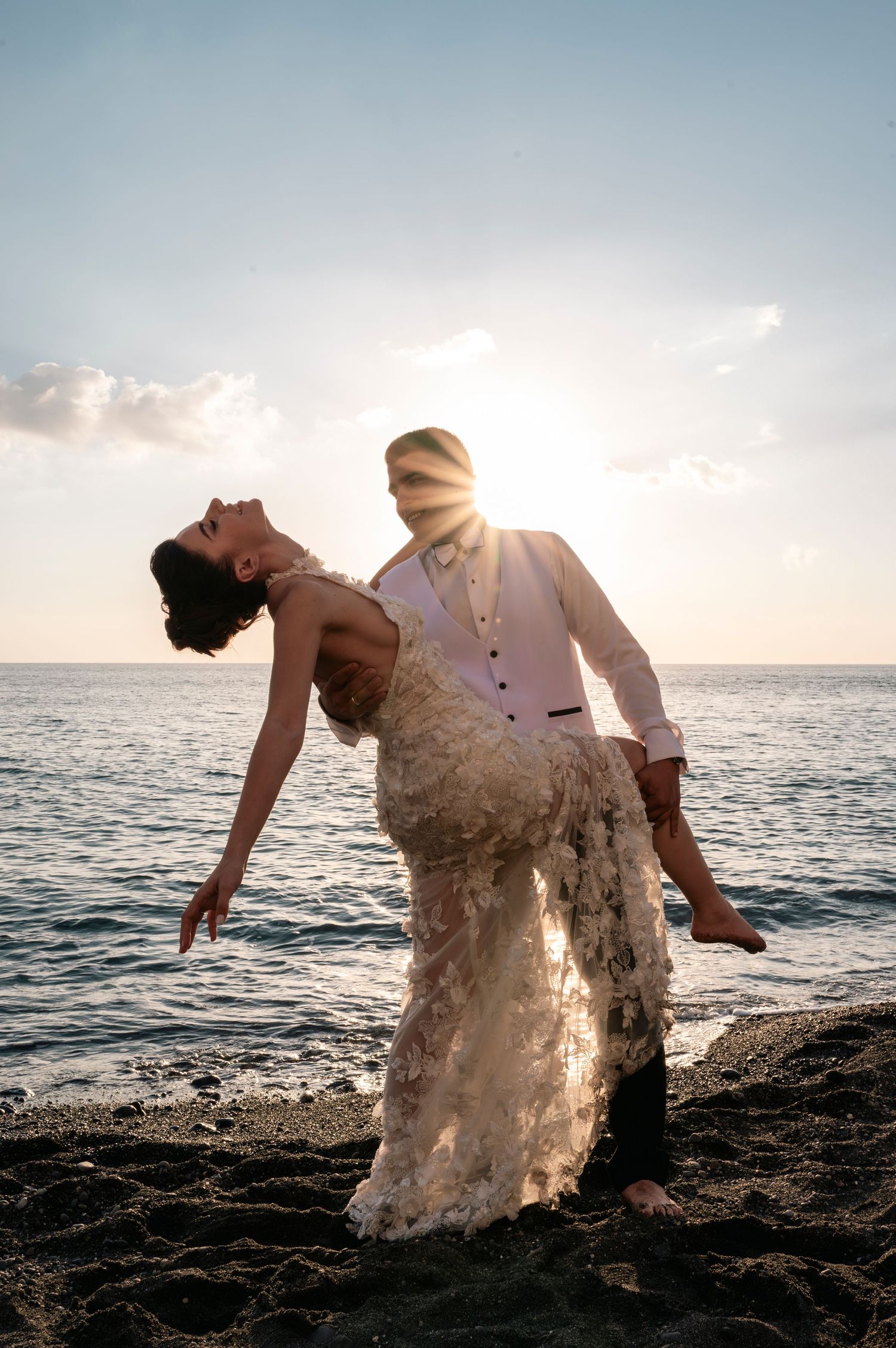 A romantic wedding photo of a couple posing dramatically against an ocean sunset.