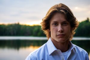 Portrait of someone in a blue button-down shirt against a serene lake backdrop at sunset.