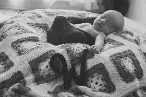 Newborn baby sleeping on a patterned knit blanket in black and white.