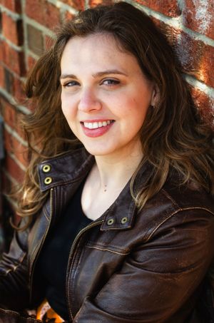 Portrait against a brick wall wearing a brown leather jacket.