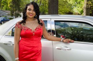A person wearing a stunning red formal dress poses elegantly next to a silver luxury car.