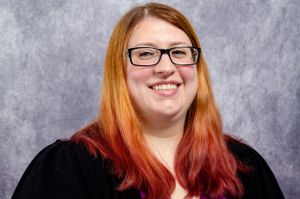 Professional headshot of someone with red hair wearing glasses and dark clothing.