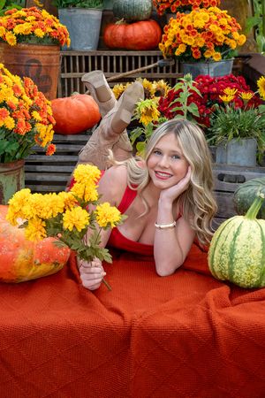 Colorful fall scene with orange pumpkins, marigolds and chrysanthemums displayed on a red blanket.