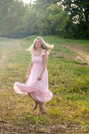 A person in a flowing pink dress twirls gracefully across a sunlit meadow at golden hour.