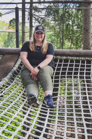 Someone relaxing on a rope net structure outdoors wearing casual attire and a baseball cap.