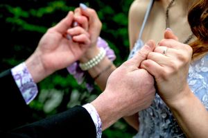Close up of hands holding each other during a wedding ceremony with lace sleeves and bracelets visible.