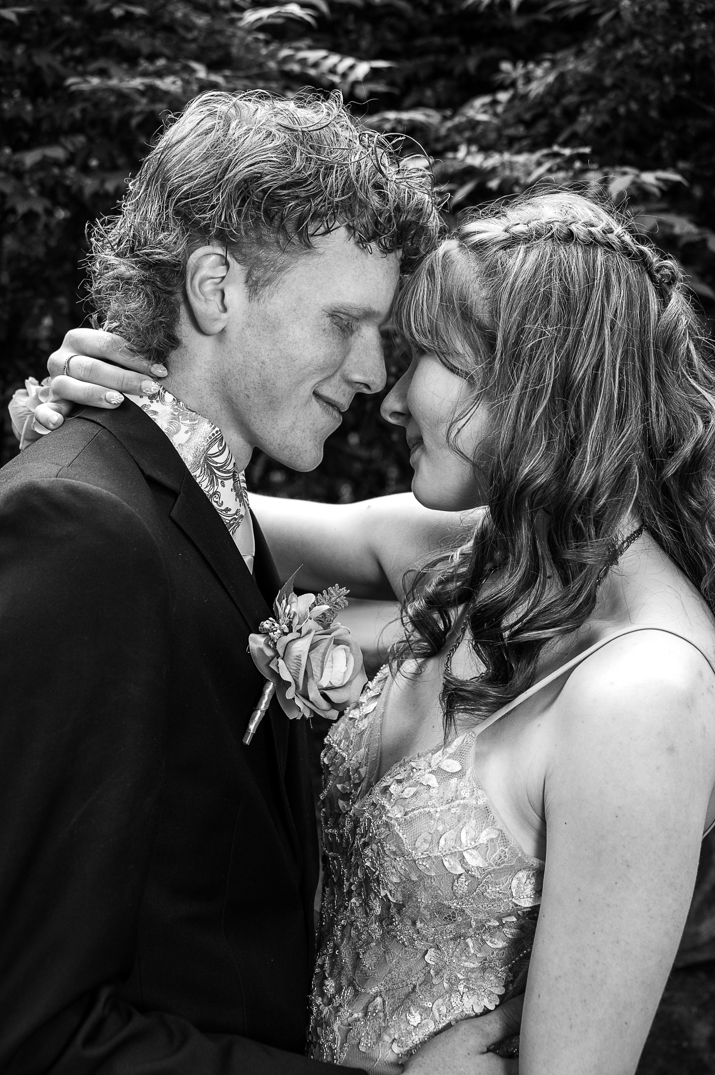 Black and white portrait of a couple in wedding attire sharing an intimate moment against a natural backdrop.