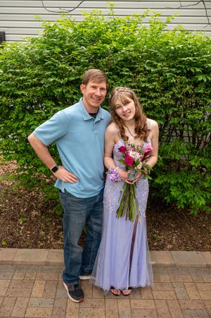 A couple poses together outdoors, with one wearing a lavender dress and holding a colorful floral bouquet.
