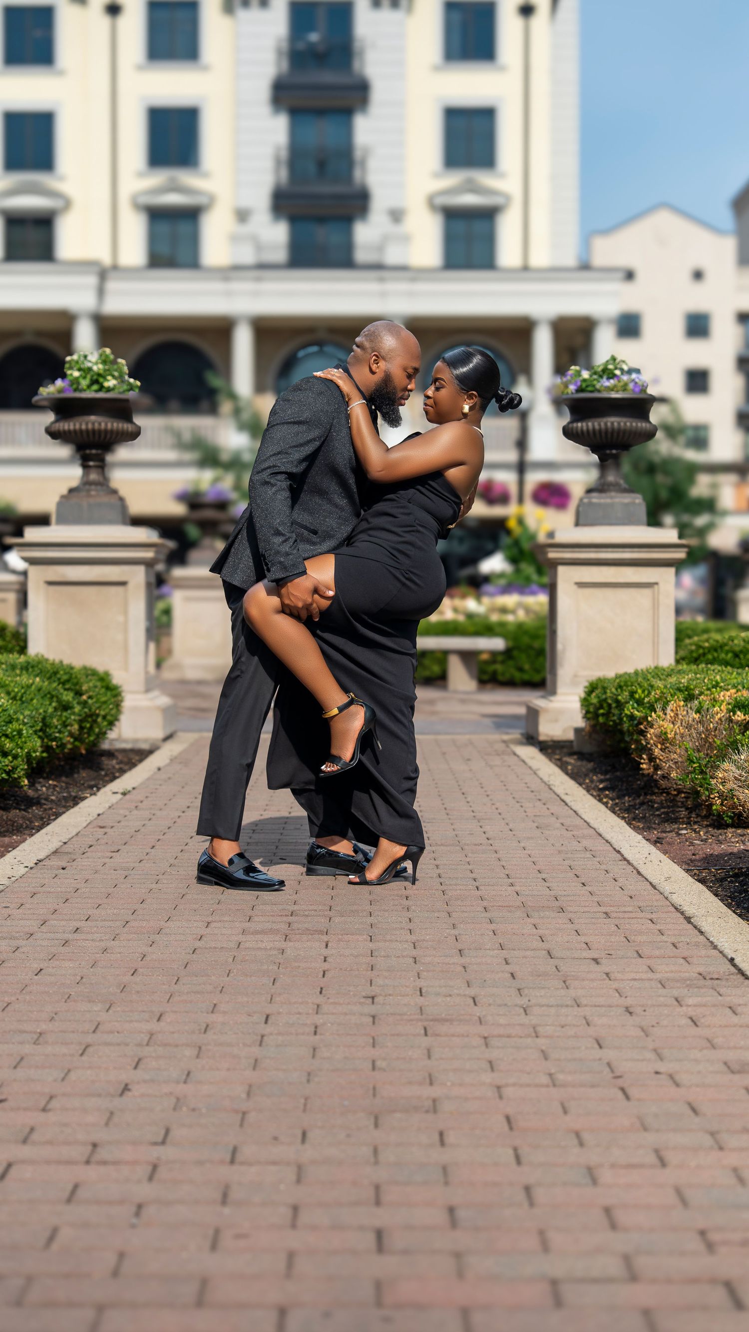 Romantic couple in formal attire embracing on a brick pathway in front of an elegant building.