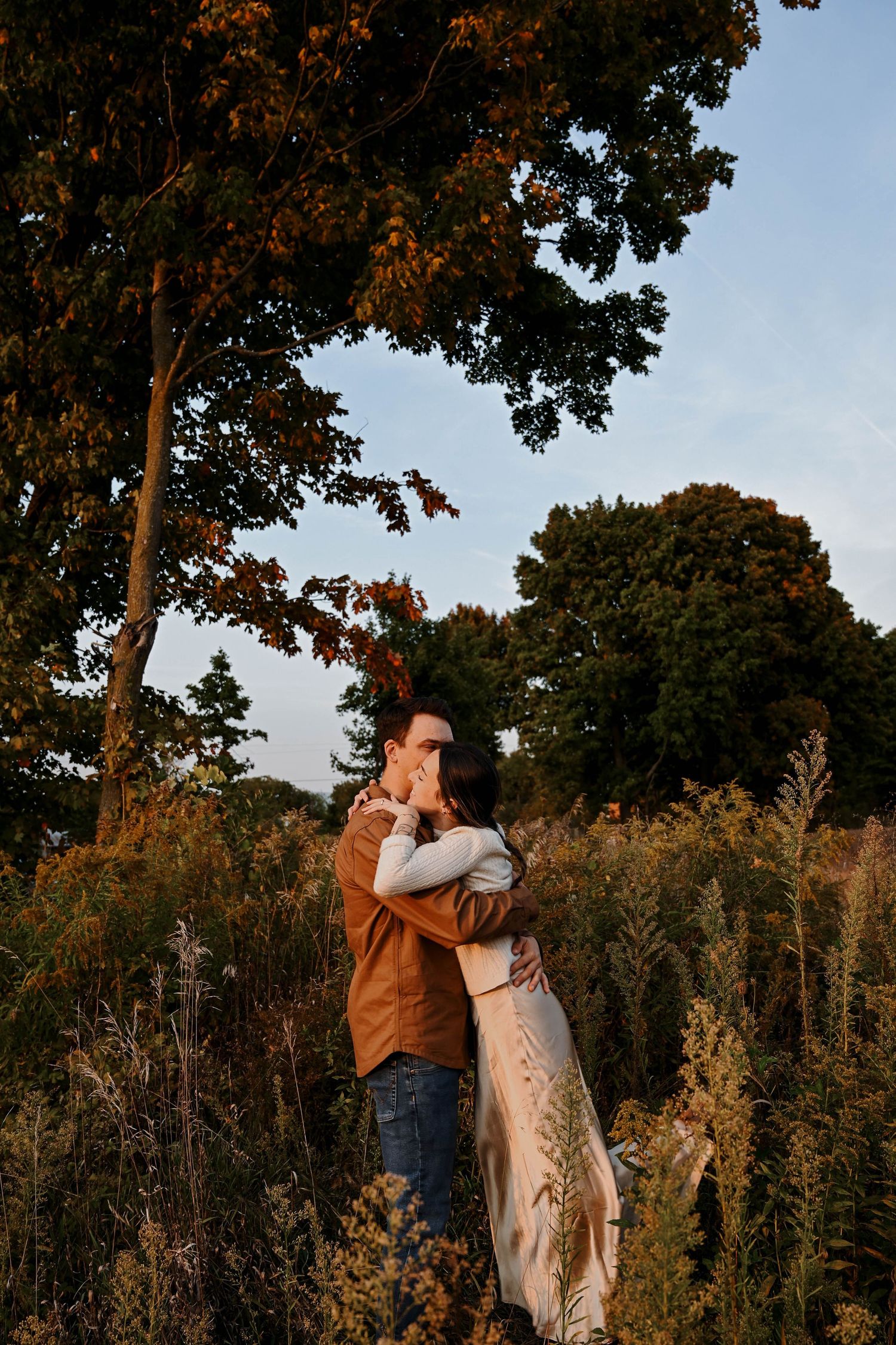 Couple embracing in tall grass field during golden hour photoshoot.