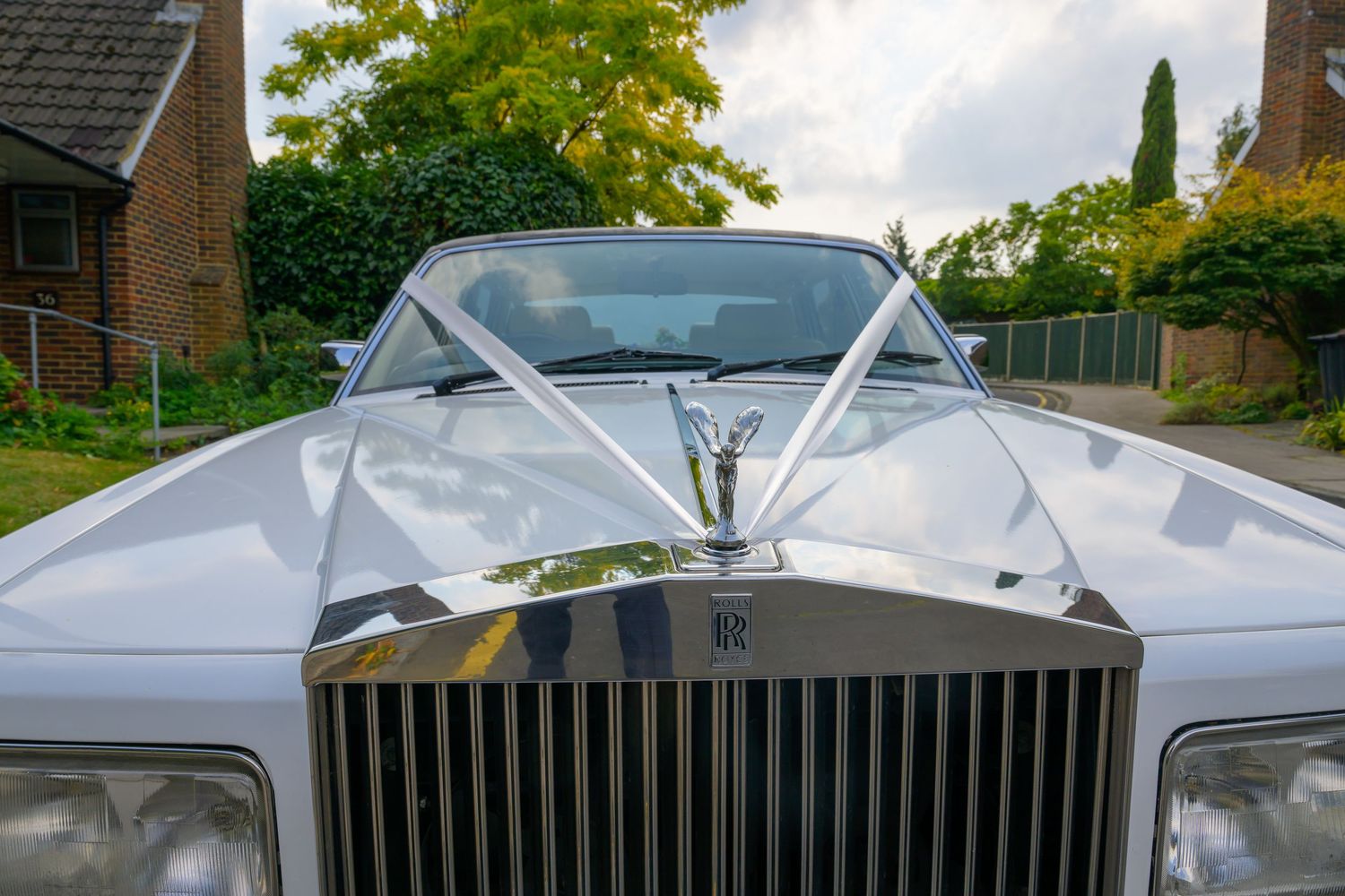 Close-up view of a white Rolls-Royce luxury car's front grille and hood decorated with wedding ribbons.