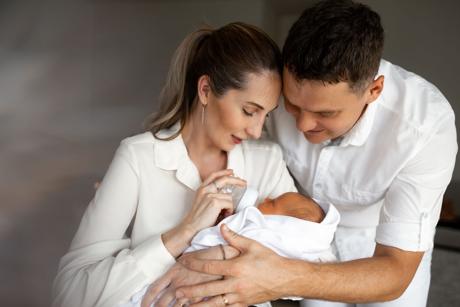 Parents in white clothing tenderly holding and looking at their newborn baby.