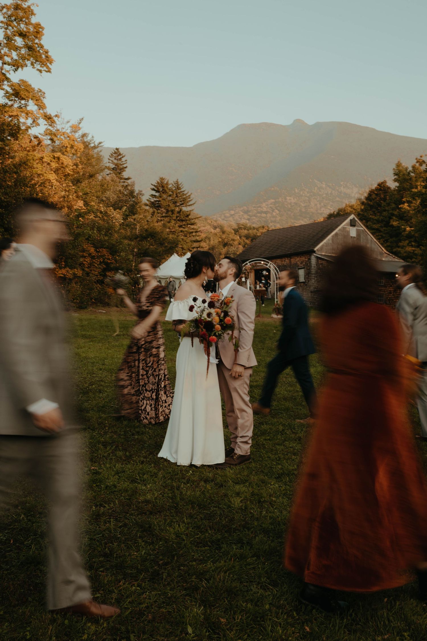 Outdoor mountain wedding ceremony with guests in warm autumn colors.