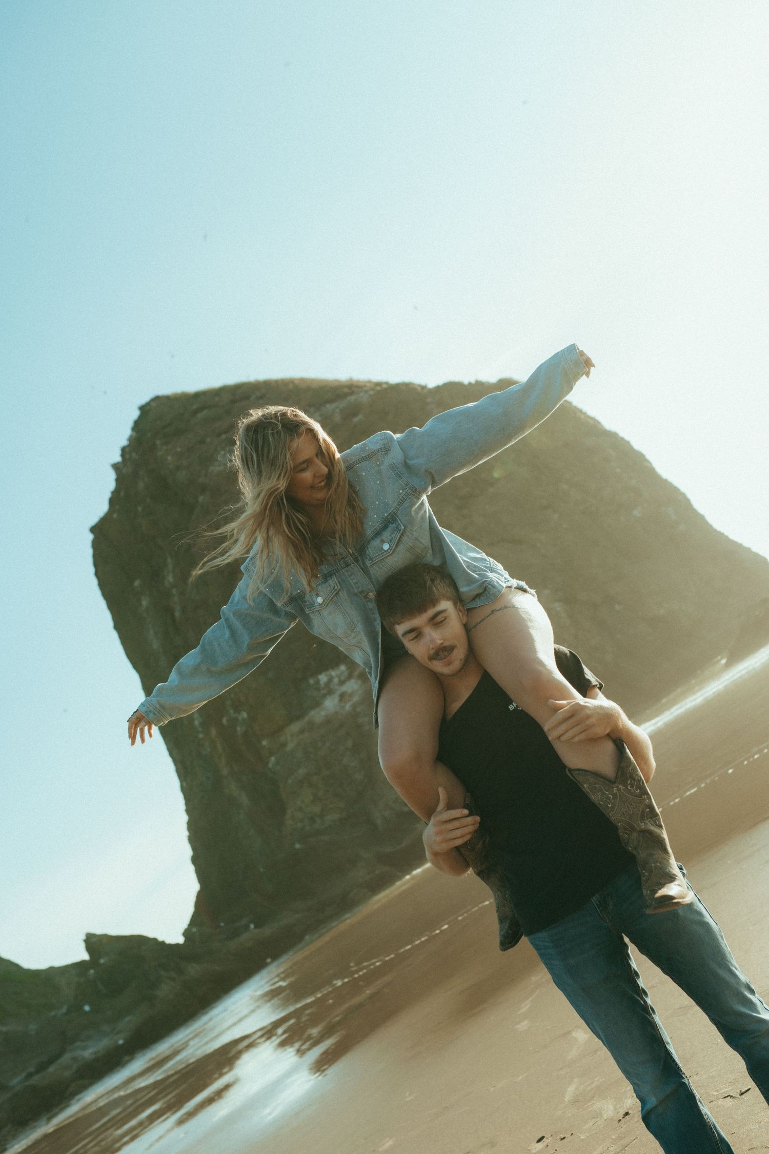 Two people share a tender moment sitting together on coastal rocks at sunset in muted golden light.