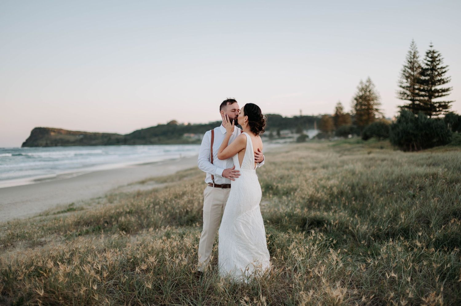A romantic wedding photo on a scenic coastal cliff at sunset with rolling hills and ocean views.