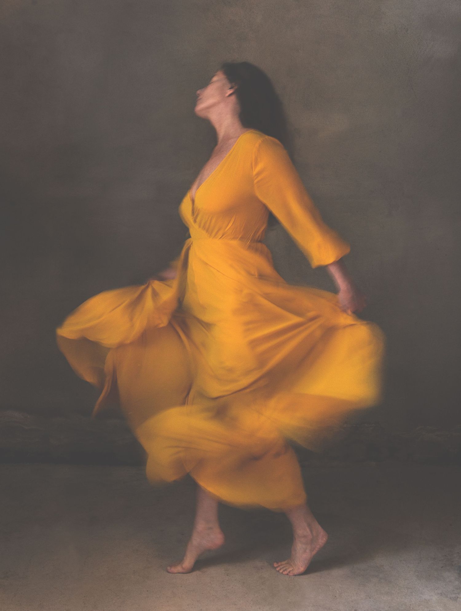 En kvinna som dansar barfota i gul klänning.