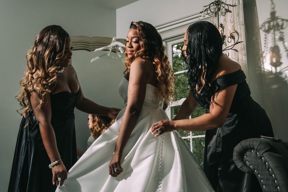 Friends help adjust a beautiful white wedding dress at a getting ready session on a wedding day.