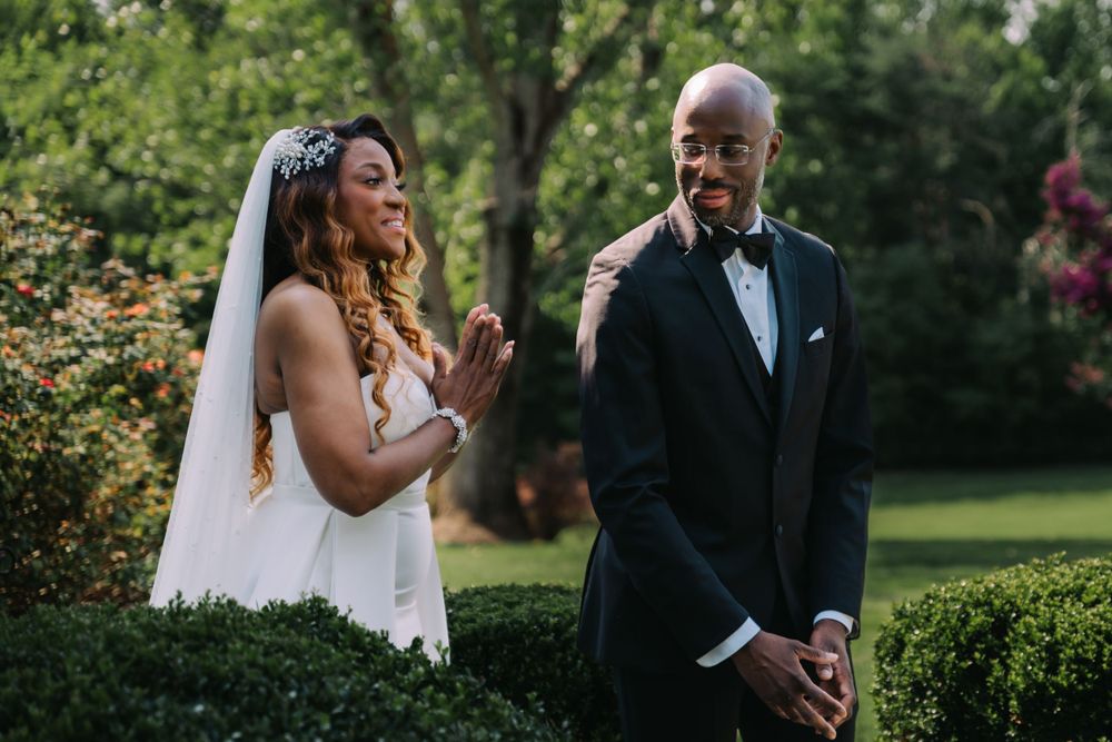 Two people share a joyful moment during an outdoor garden wedding ceremony with lush greenery in the background.
