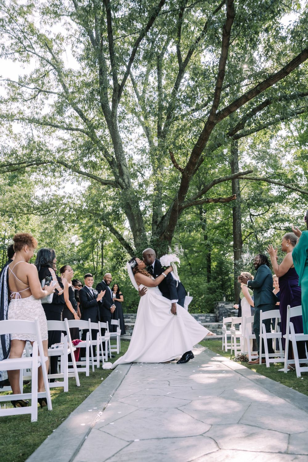 Joyful wedding ceremony moment set outdoors with white chairs and lush trees creating a natural garden backdrop.