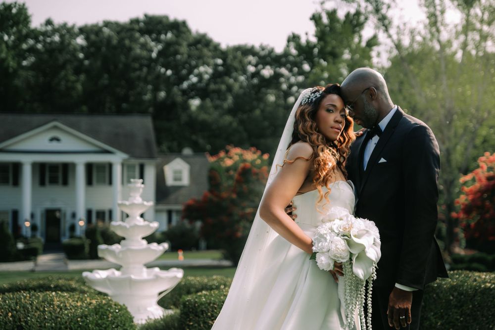 A couple shares a romantic moment in front of a white fountain at an elegant Southern estate with blooming azaleas.