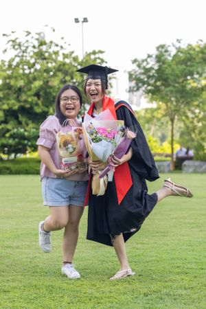 Two people celebrating graduation with flower bouquets on grass lawn.