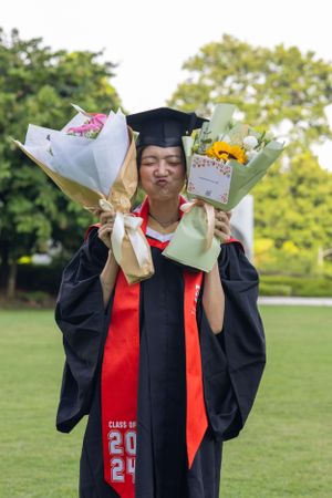 Graduate holding flower bouquets while wearing class of 2024 graduation regalia.