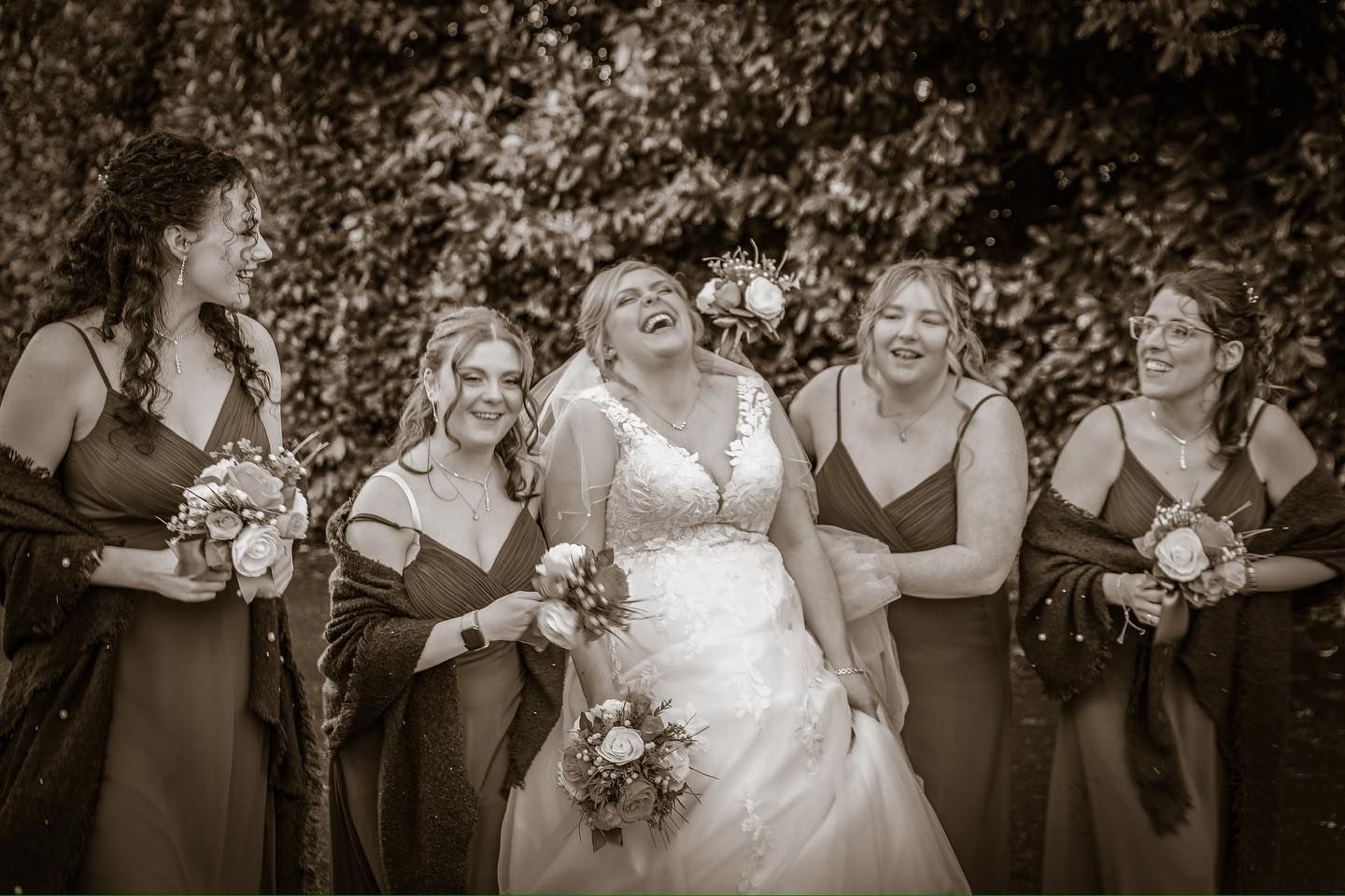 Joyful wedding party laughing together outdoors in black and white photography.