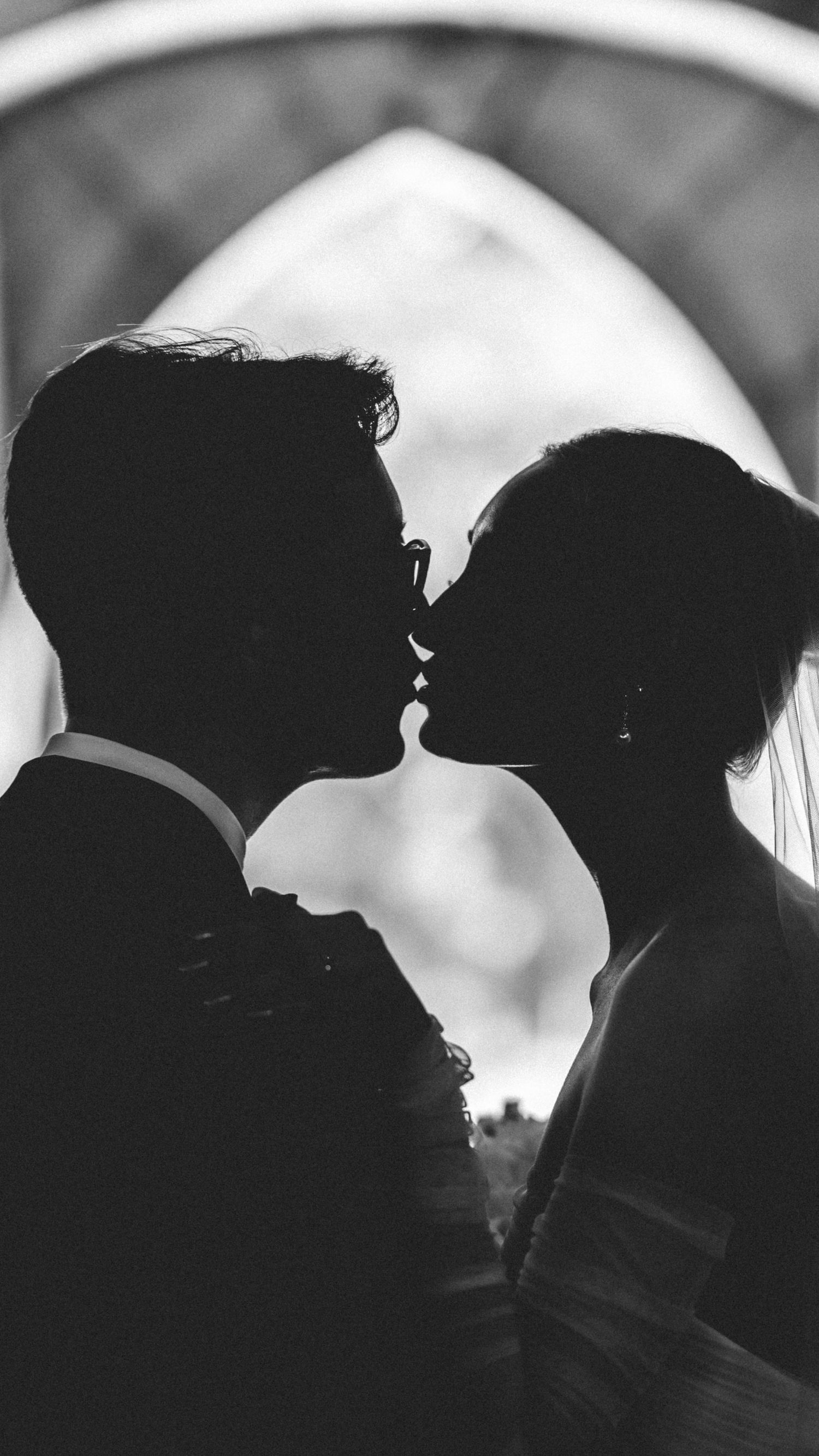 A romantic silhouette of a wedding couple sharing an intimate kiss in black and white.