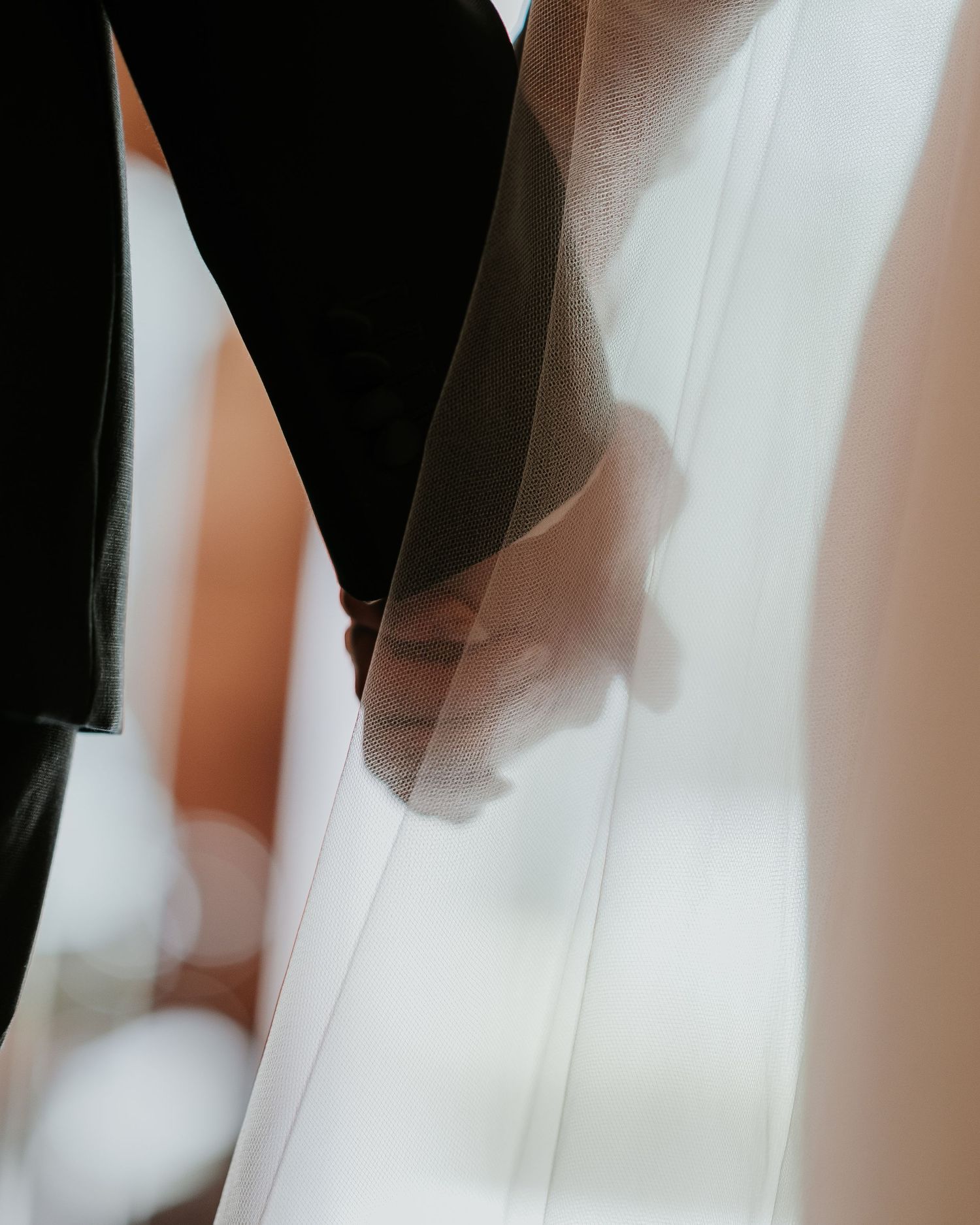 Close-up detail of flowing white wedding dress fabric and dark suit creating abstract shapes.