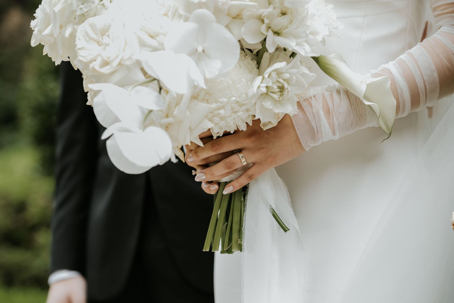 White bridal bouquet with hydrangeas held by gloved hands against a wedding dress.