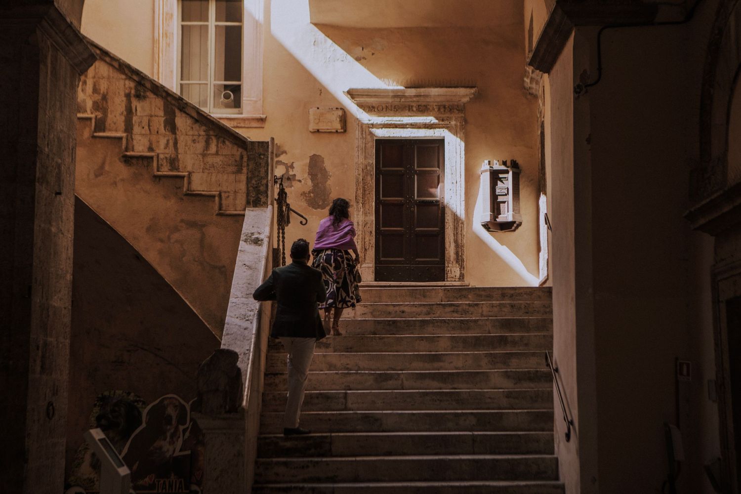 Wedding couple ascending stone staircase in historic European building.