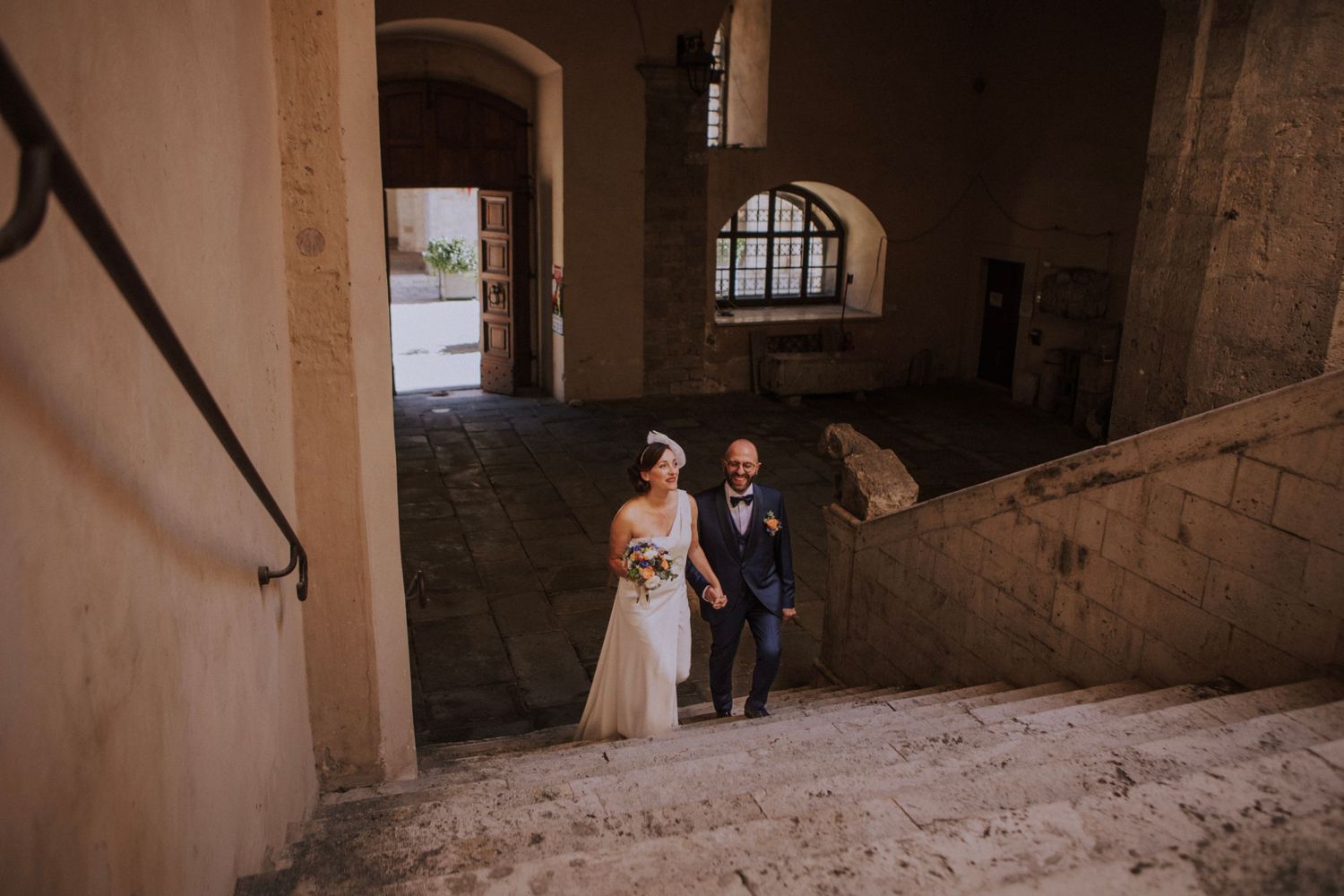 Couple walking through arched stone passageway during wedding ceremony.