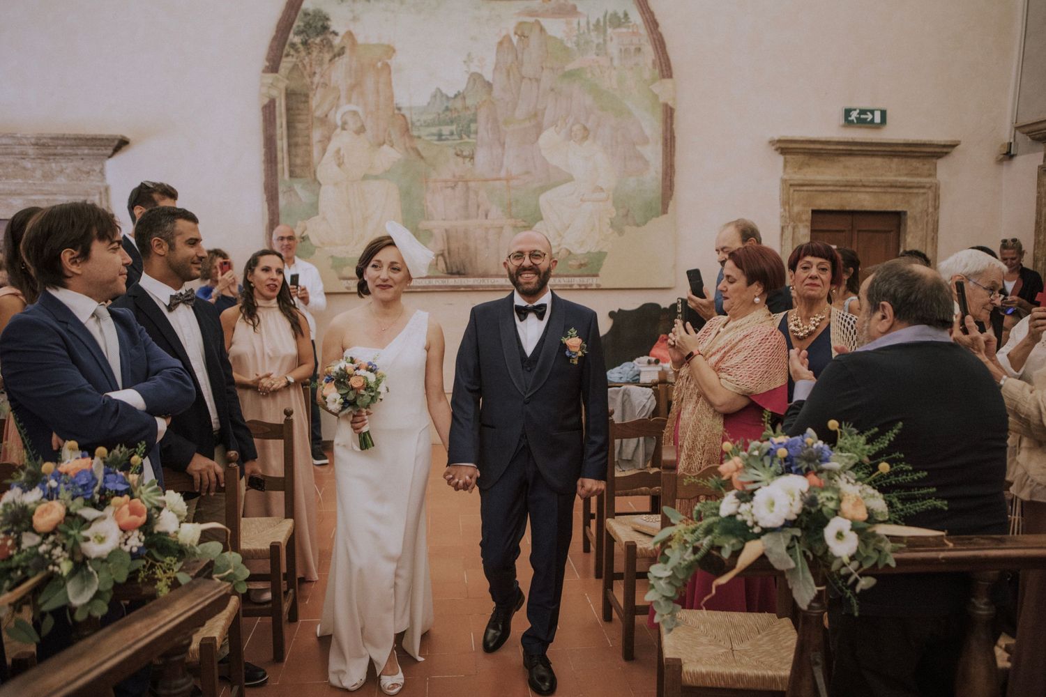 Wedding ceremony in historic chapel with floral arrangements and guests.