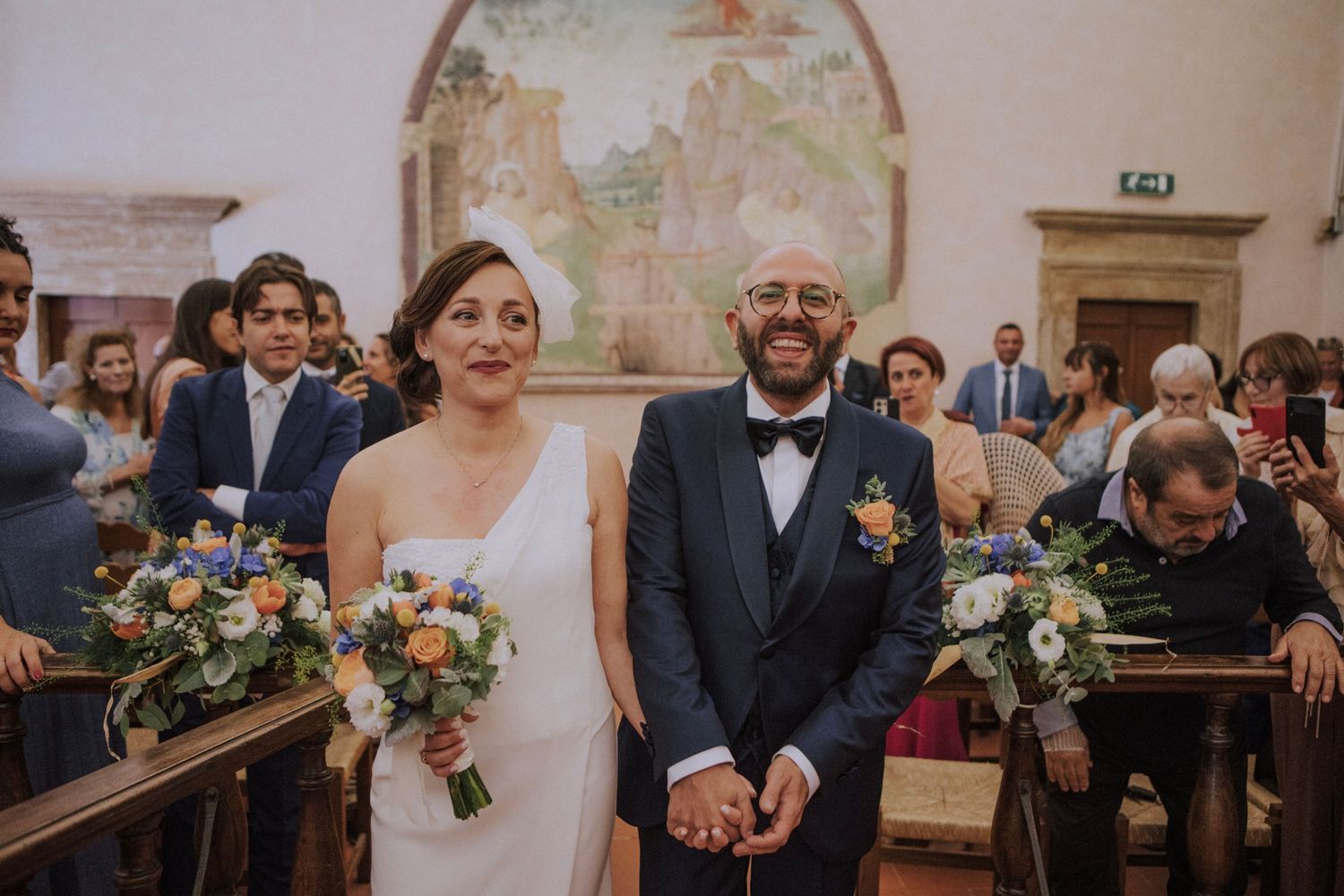 Joyful wedding ceremony moment in historic chapel with fresco artwork.