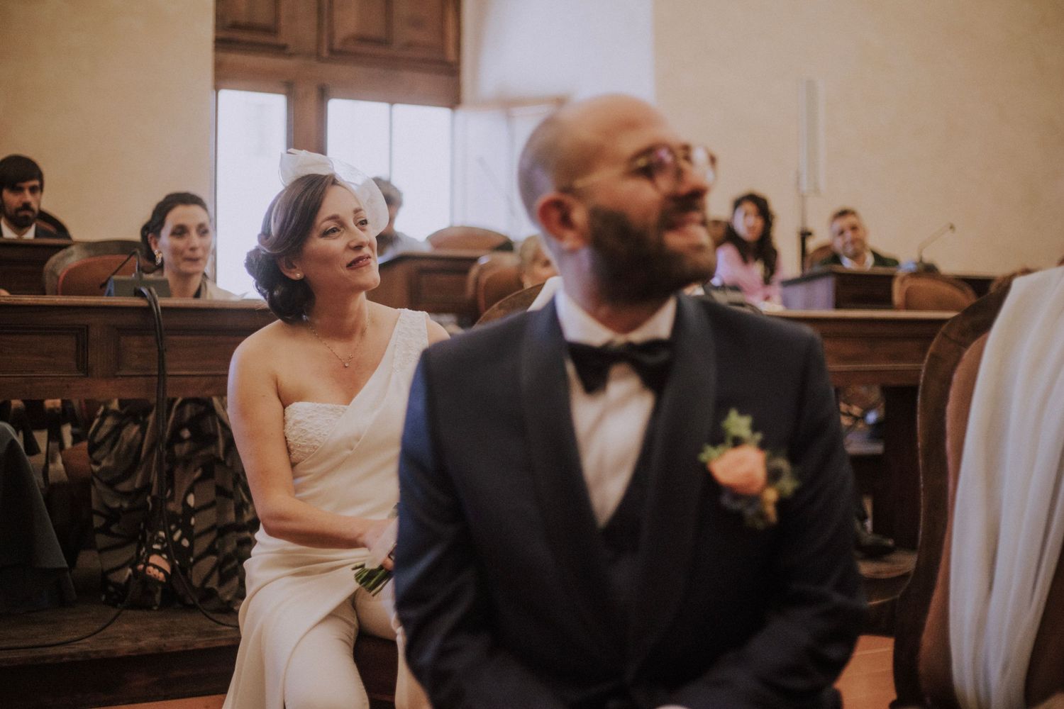 Guests seated in wooden church pews during a ceremony with light filtering through the windows.