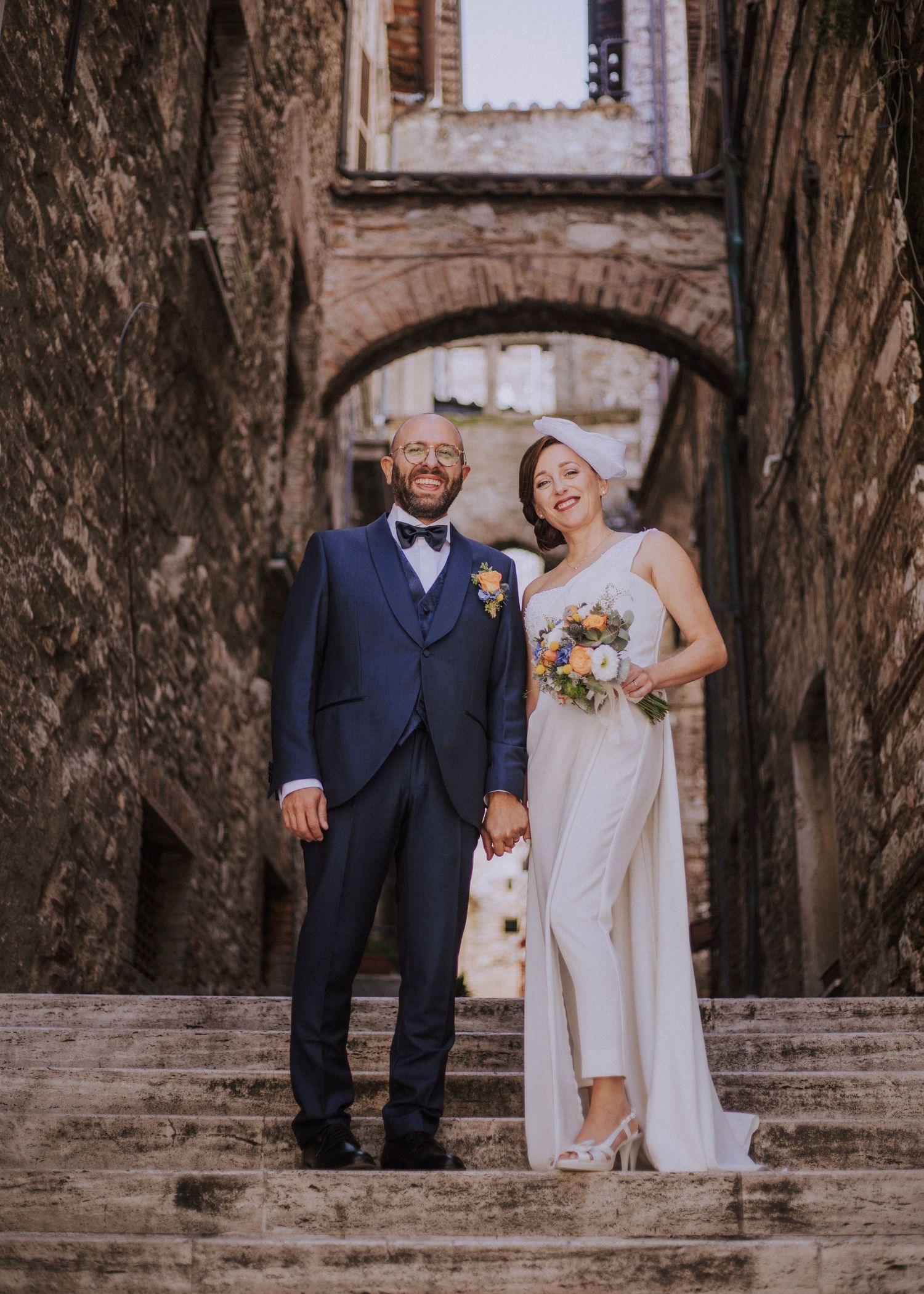 Wedding couple posing under stone archway in medieval alley.