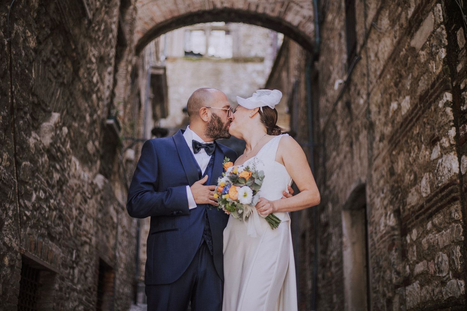 Romantic wedding moment captured in historic stone alleyway with elegant floral bouquet.