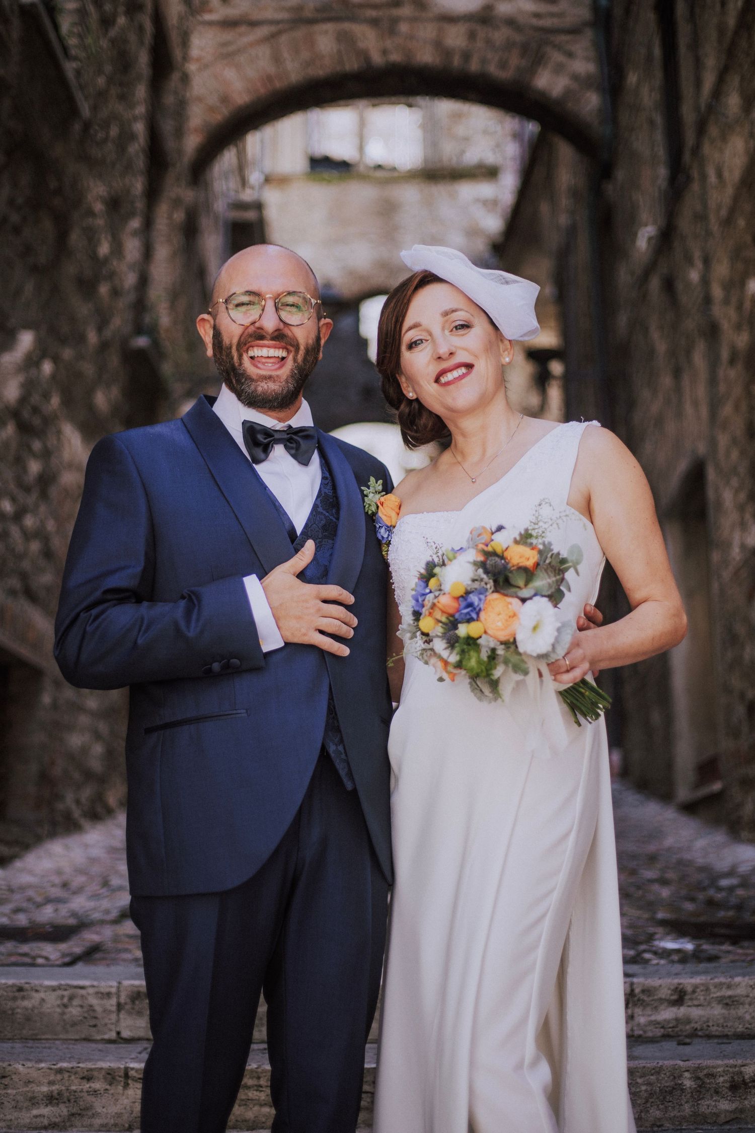 Joyful wedding portrait in rustic stone passage with colorful spring bouquet.