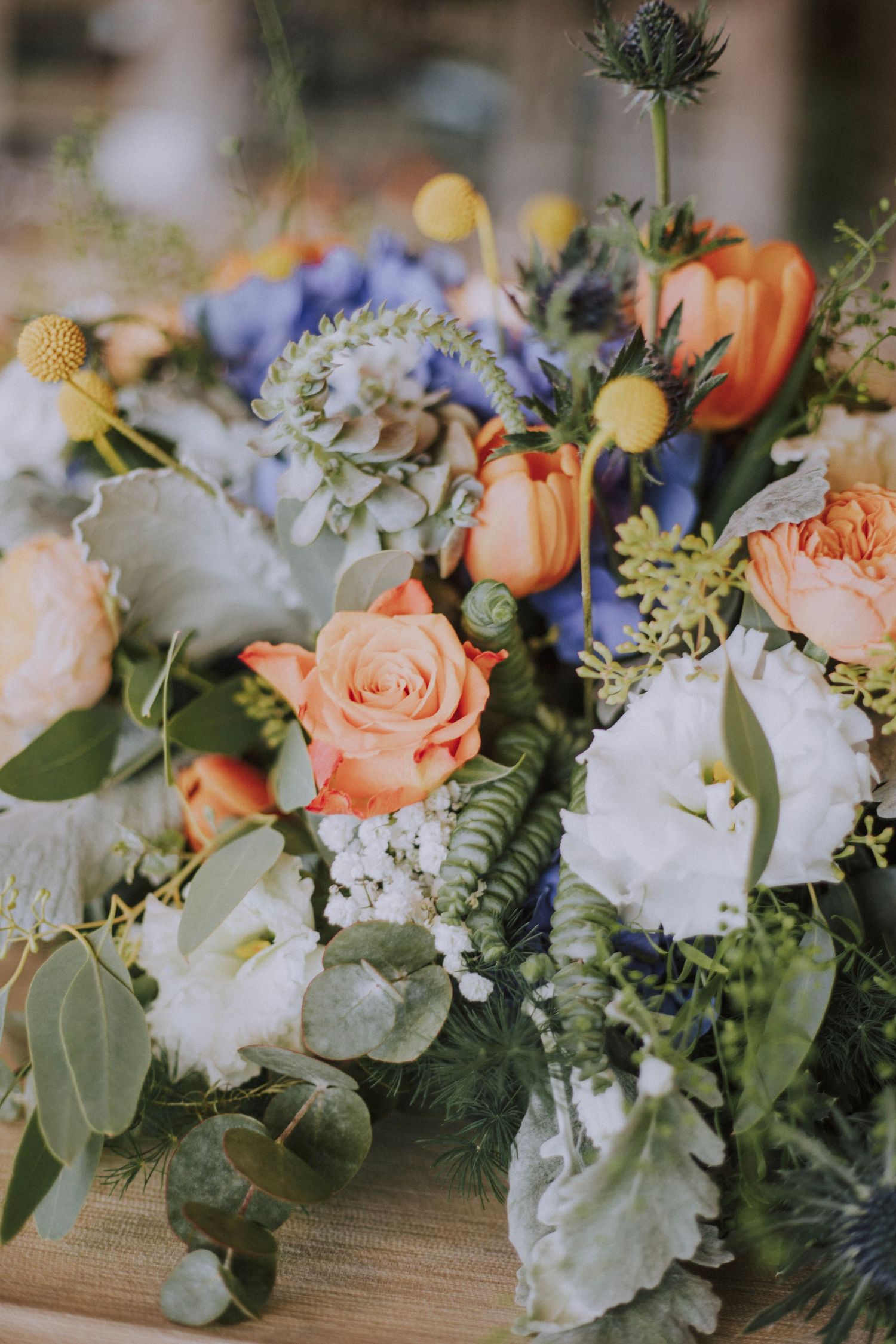 Elegant floral arrangement with peach roses, blue hydrangeas, and white flowers on wooden surface.