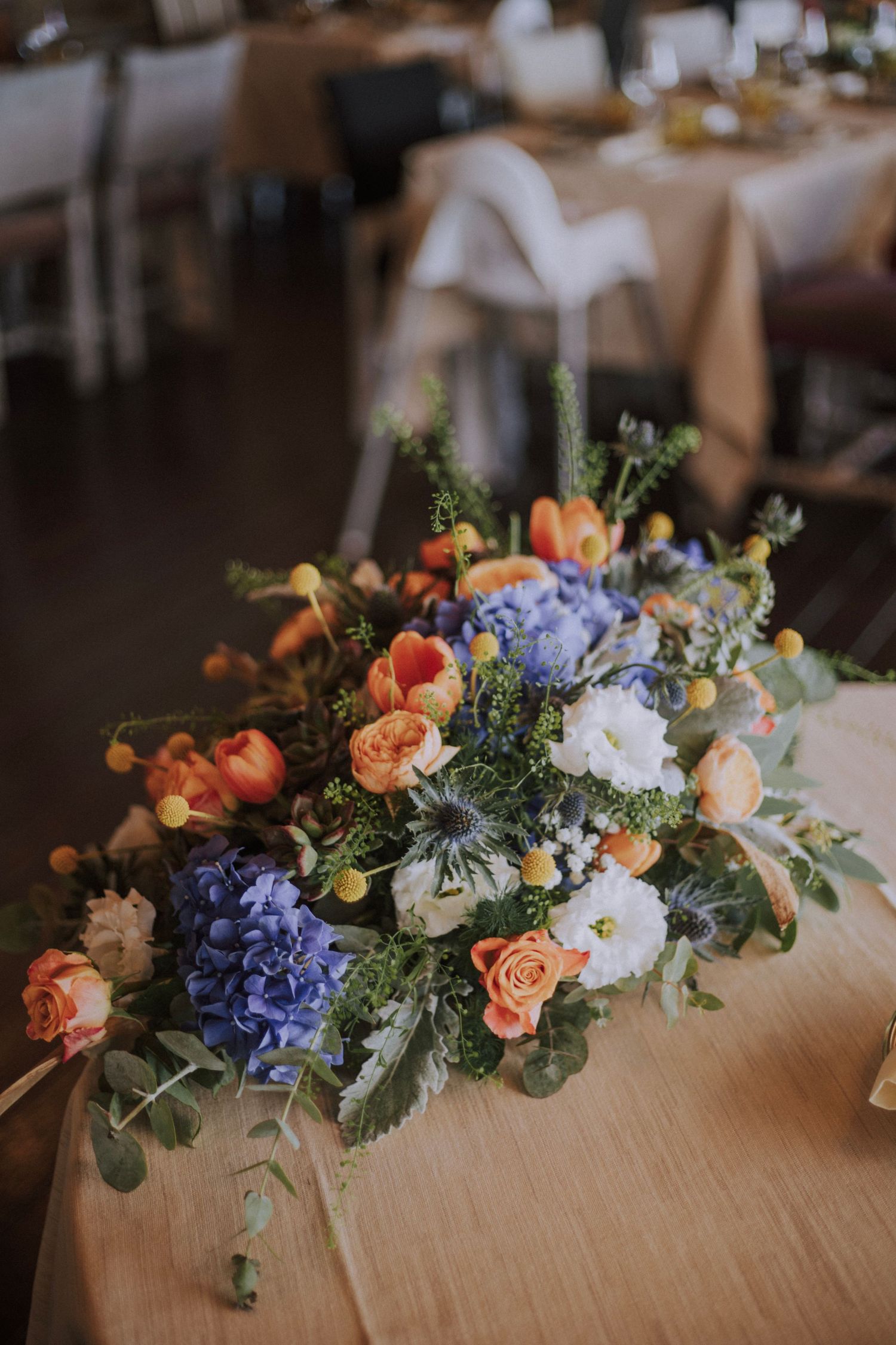Colorful wedding centerpiece featuring hydrangeas, roses and mixed flowers on reception table.