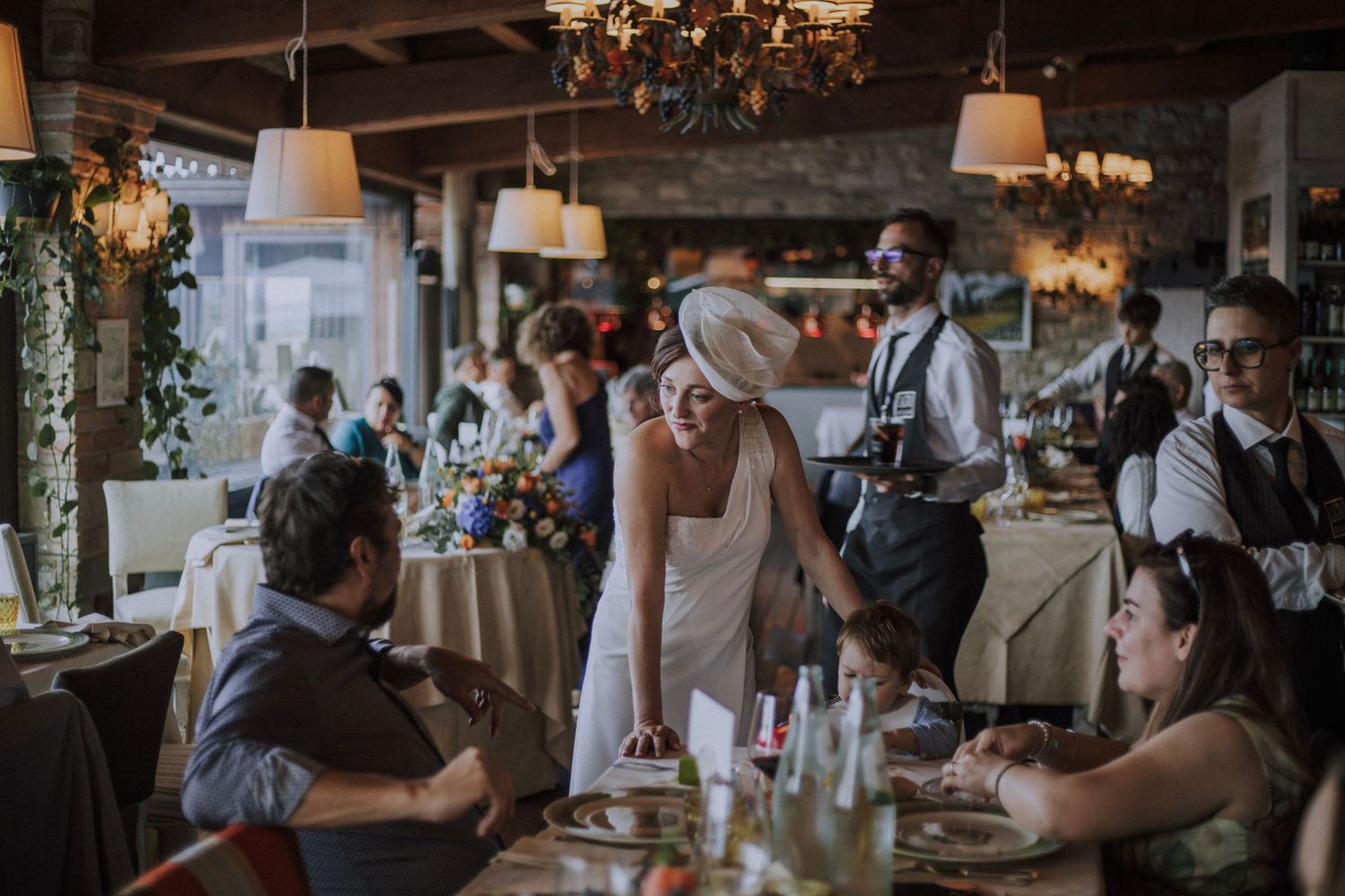 Wedding celebration with guests dining at decorated tables in rustic indoor venue.