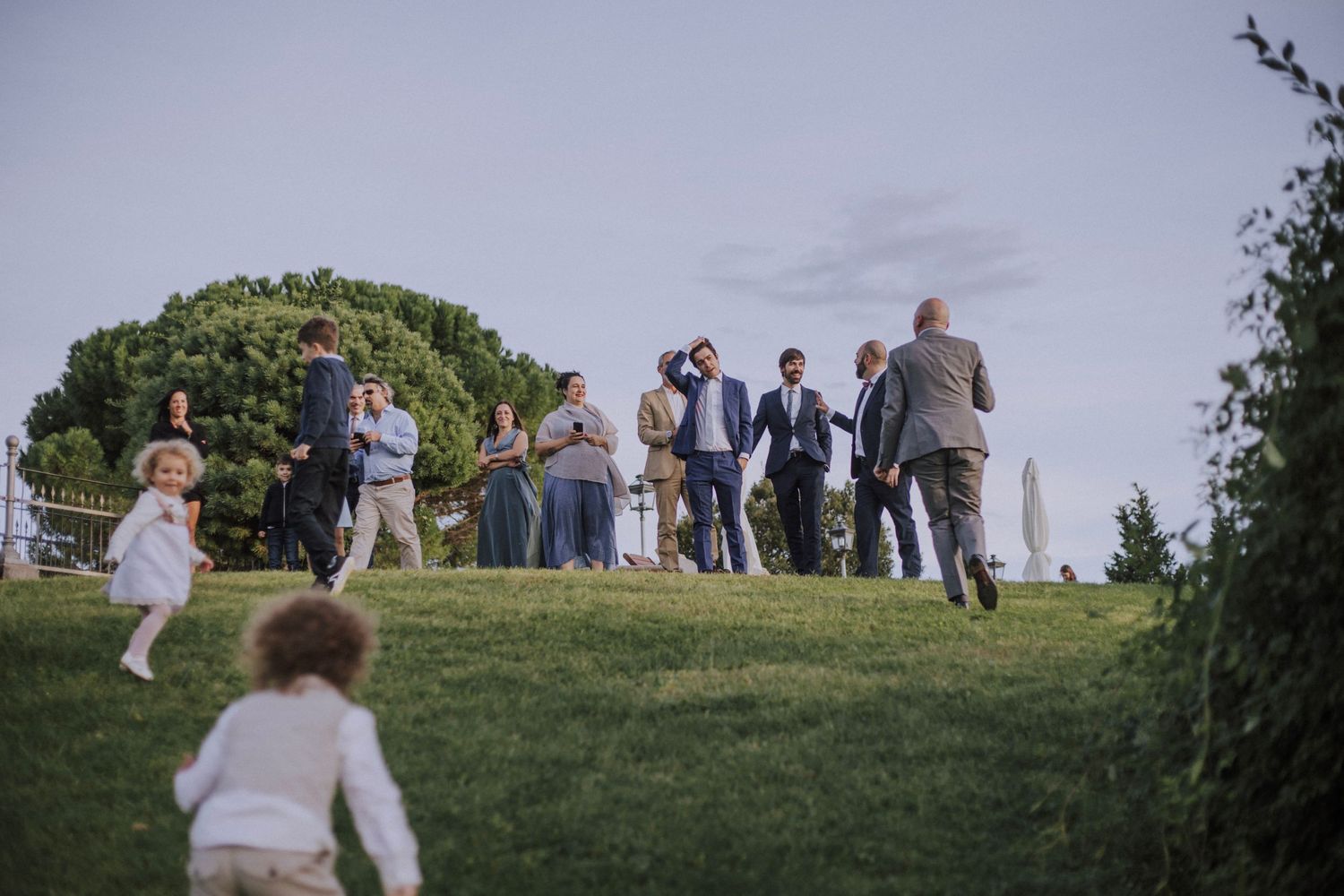 Wedding guests gathered on a hilltop lawn during an outdoor celebration.