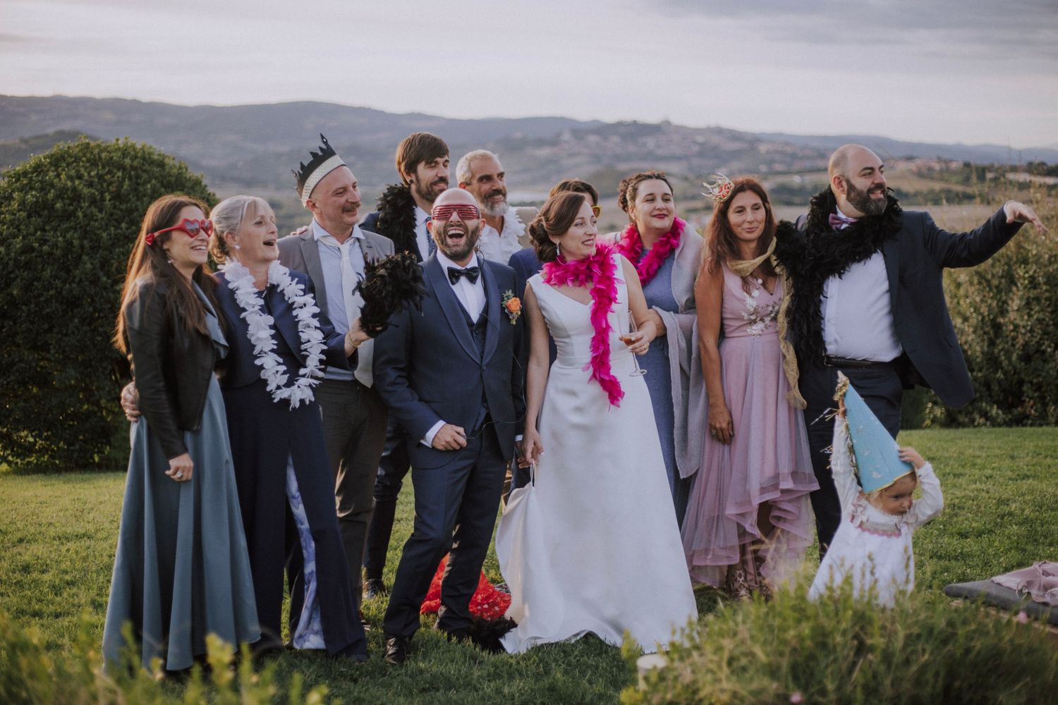 Wedding party poses joyfully on a hilltop during an outdoor celebration at sunset.