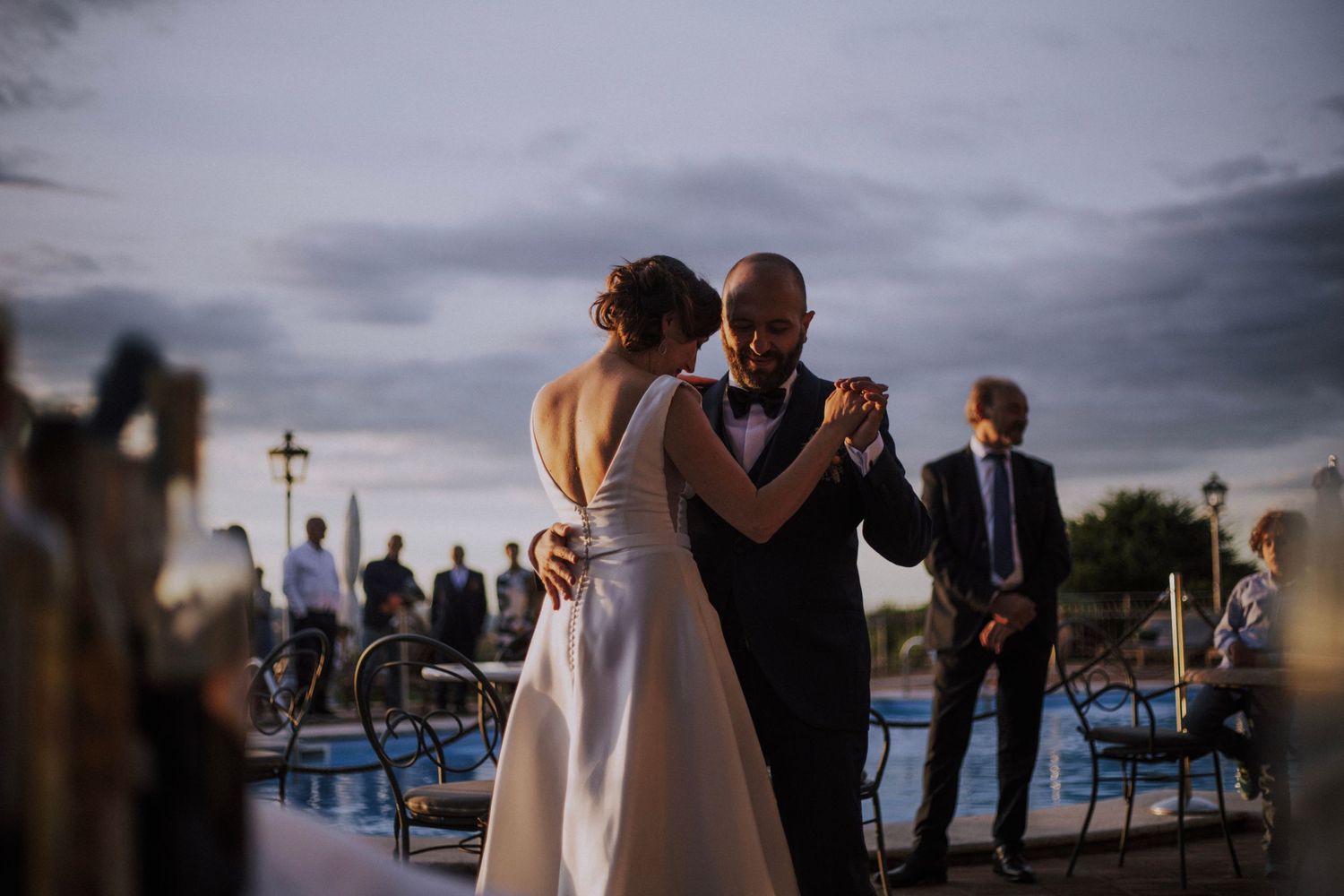 Couple dances together at dusk with waterfront and lighthouse visible in background.
