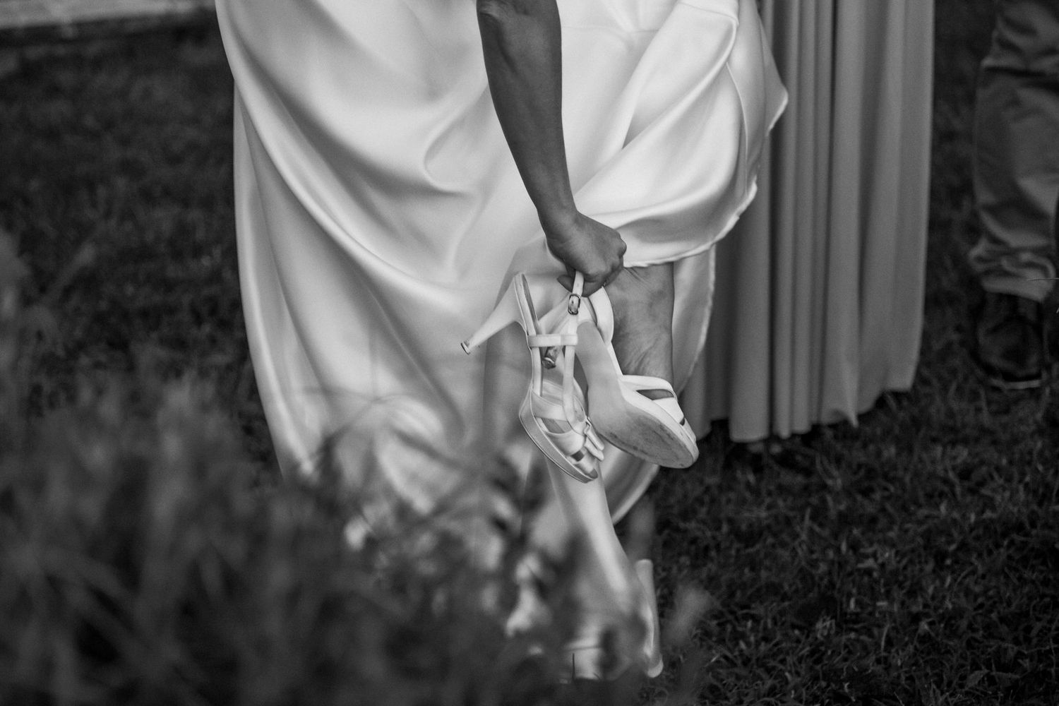 Black and white detail shot of bride's wedding shoes being held against dress.
