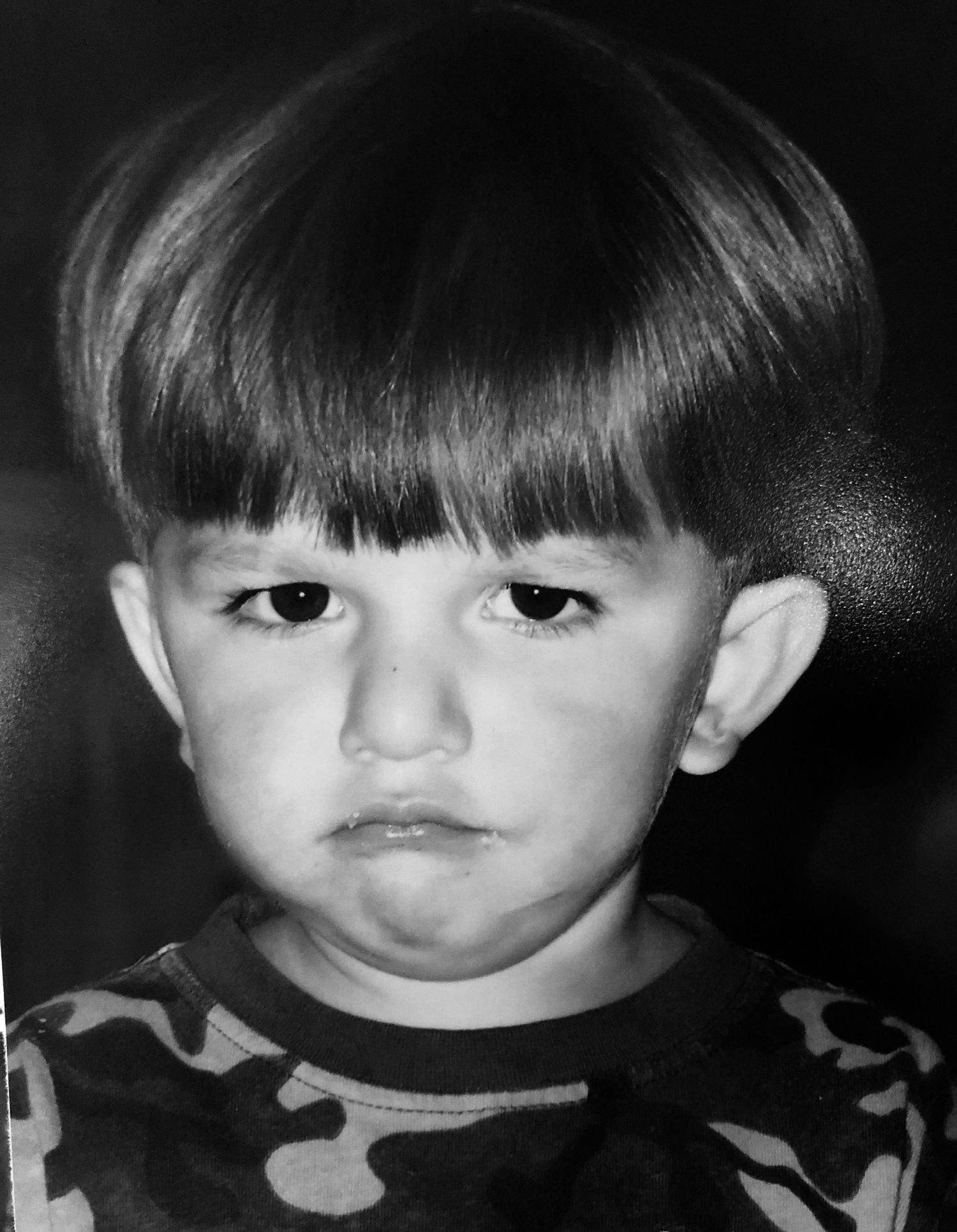 Black and white close-up portrait of a young child wearing camouflage.