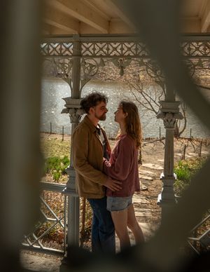 Romantic couple embracing inside an elegant white gazebo with a serene lake visible in background.
