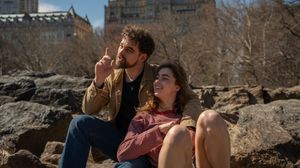 Young couple sitting on rocks in Central Park, man pointing upward while woman laughs joyfully.